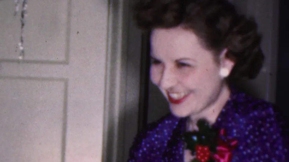 The final frame shows the woman smiling toward someone off-camera, with styled dark hair, pearl earrings, and a holiday brooch visible against a private interior doorway.