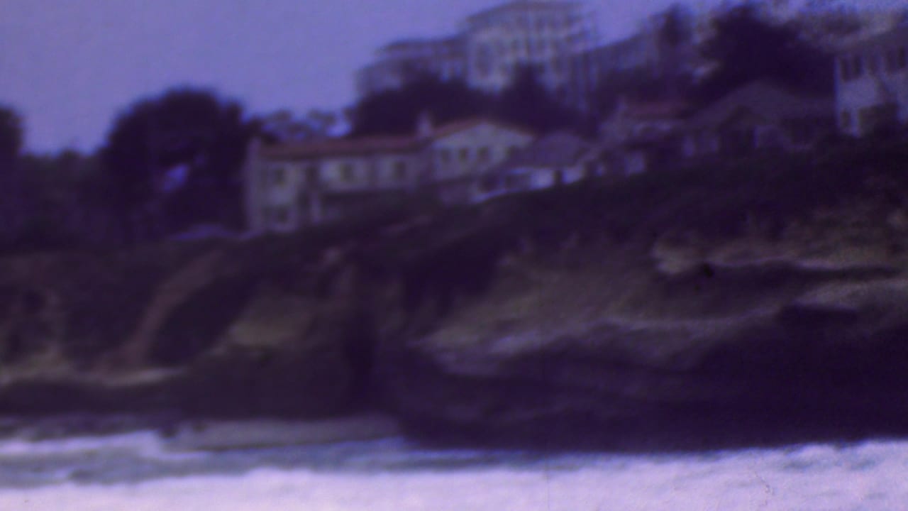 1953 home-movie frame identified as Cleveland, Ohio, showing soft-focus buildings and trees on a coastal bluff above foaming water.