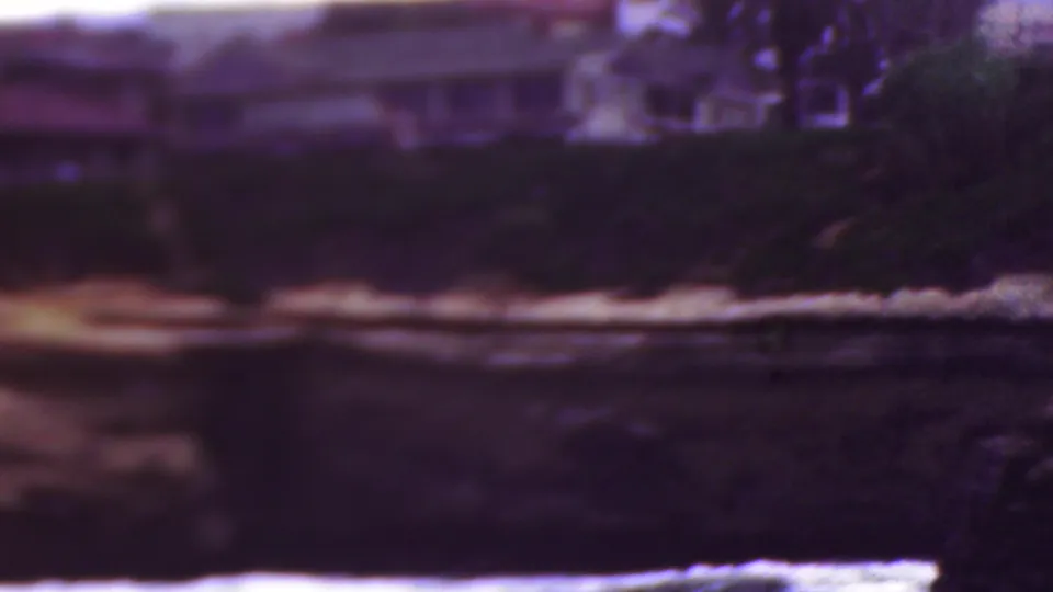 1953 Cleveland, Ohio 8mm view of a hazy shoreline with low buildings and trees above dark water and a bright surf line.