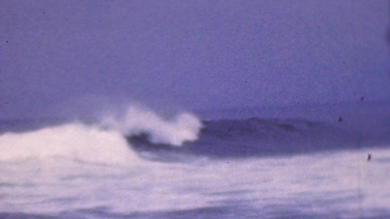 1953 8mm home-movie frame associated with Cleveland, Ohio, showing surf breaking beneath a dark horizon and muted purple-blue sky.