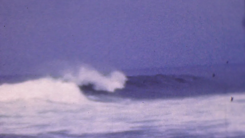 1953 8mm home-movie frame associated with Cleveland, Ohio, showing surf breaking beneath a dark horizon and muted purple-blue sky.