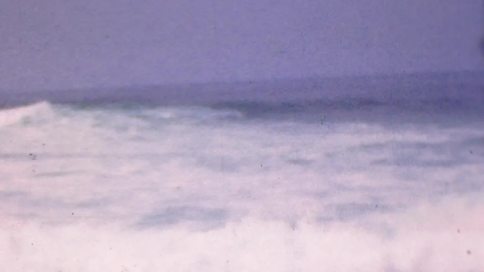1953 8mm home-movie frame associated with Cleveland, Ohio, showing soft, blurred wave texture and pale foam below a muted horizon.