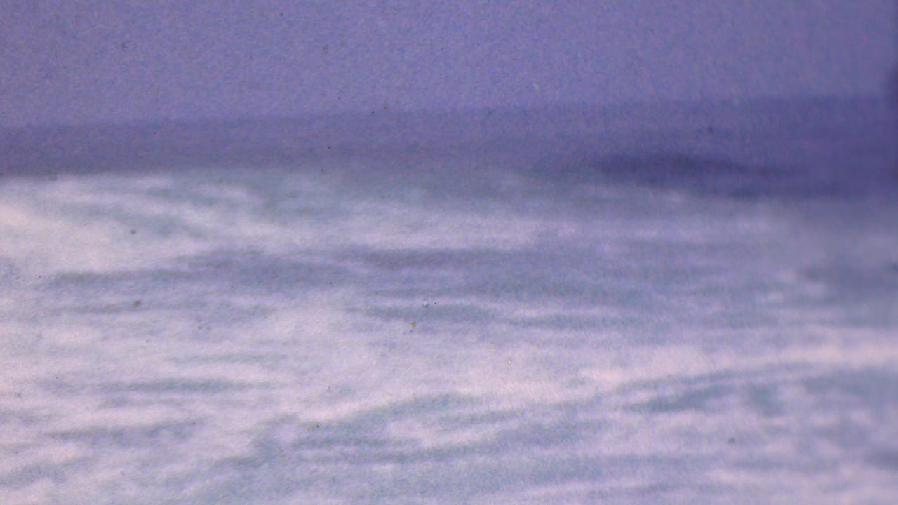 Blurred rolling water with a pale horizon and cloudy sky.