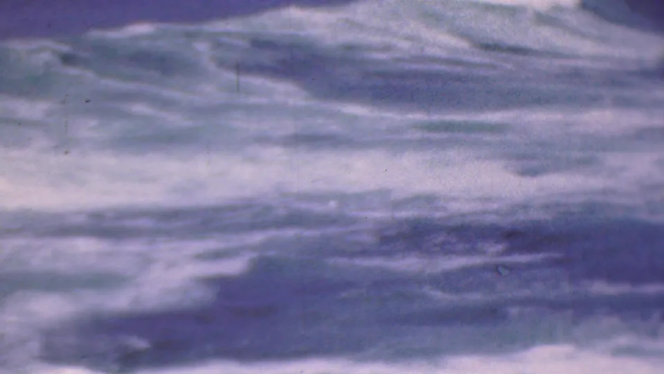 Turbulent open water fills the frame, with soft white foam streaks, blurred movement, and faded mid-century home-movie color.
