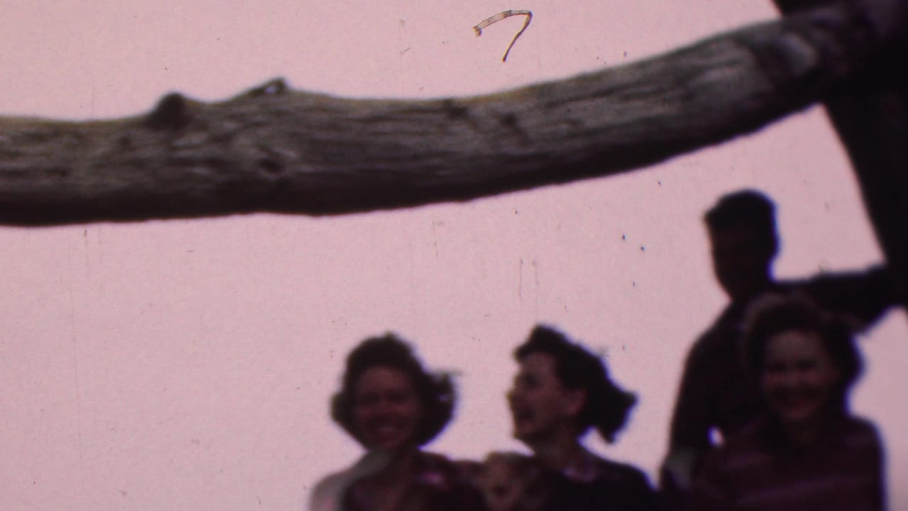 Several adults stand near a large tree branch, with women smiling below it.