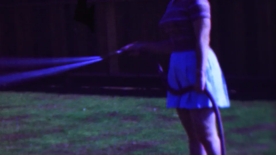 The final frame shows the woman in profile near the fence, holding the garden hose as a bright stream of water sprays across the Cleveland lawn.
