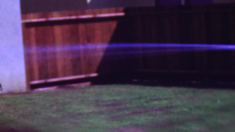 The final frame emphasizes the hose stream spraying over the lawn, with the wooden fence and only a partial view of the woman at the edge.