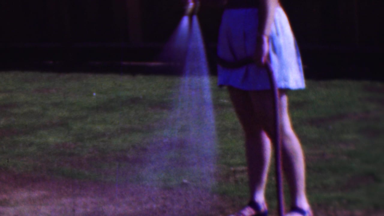 Woman stands with a hose as a cone of water falls onto the grass near her feet.