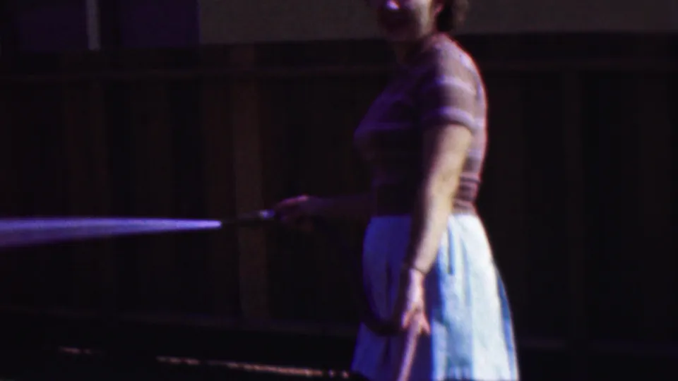 Near the end of the clip, the woman holds the garden hose low at her side while water sprays across the Cleveland yard in front of the wooden fence.