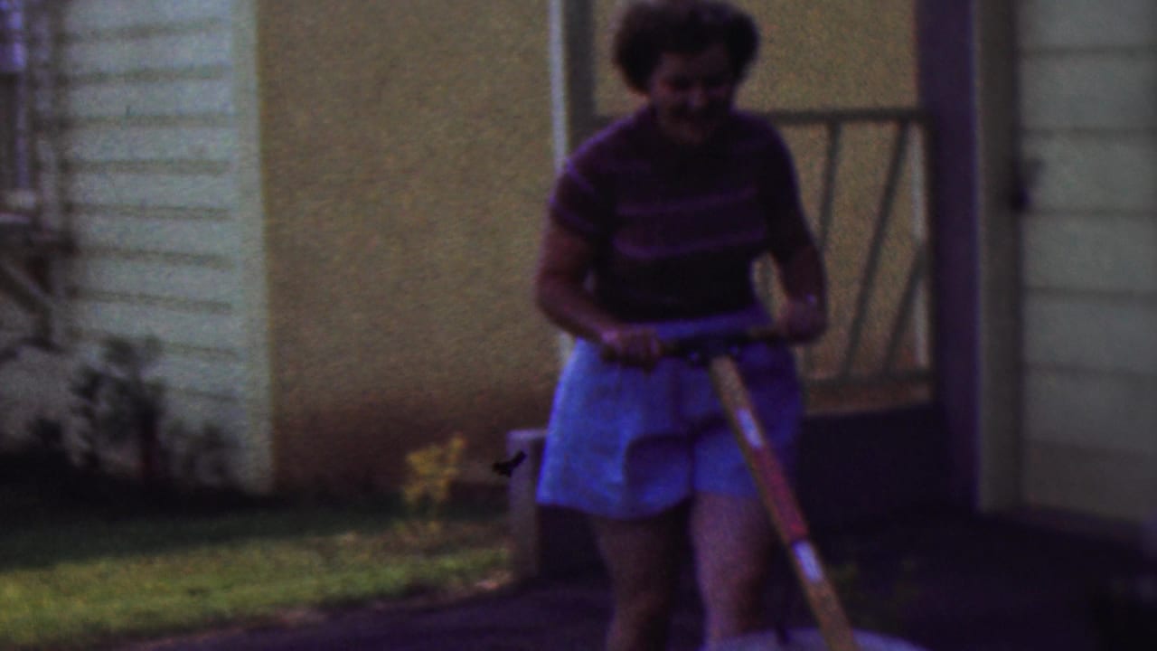 Smiling woman moves forward with a wheelbarrow in front of house siding.