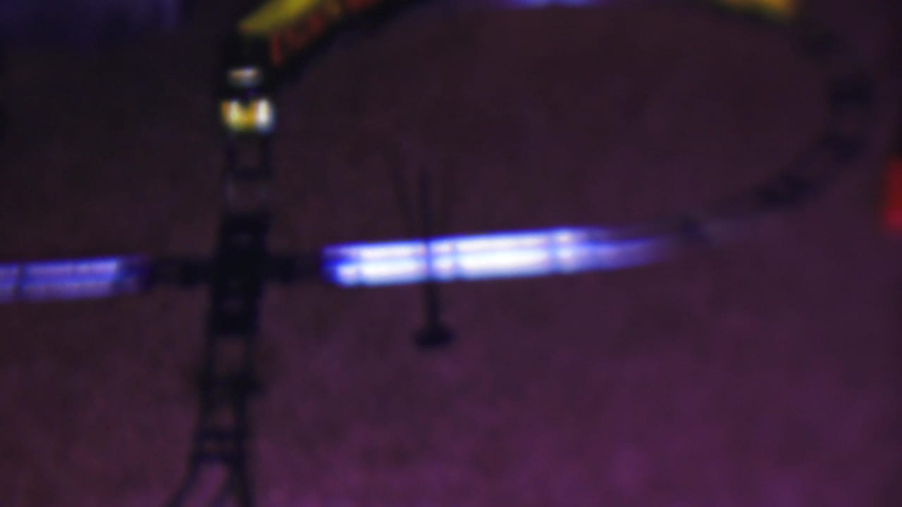 A 1953 Cleveland home-movie frame shows a curved toy train track on a carpeted floor, with blue light reflecting along the rails and a partial yellow train near the upper edge.
