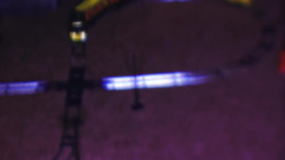 A 1953 Cleveland home-movie frame shows a curved toy train track on a carpeted floor, with blue light reflecting along the rails and a partial yellow train near the upper edge.