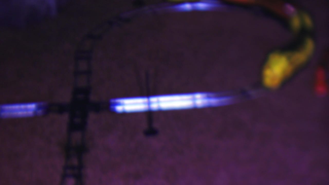 Curved toy train track on carpet with a blurred yellow locomotive near the upper right.