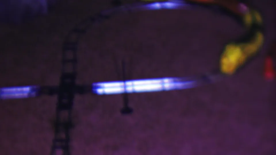 A yellow toy locomotive appears near the edge of the frame as the curved track catches blue light across a dim carpeted interior.
