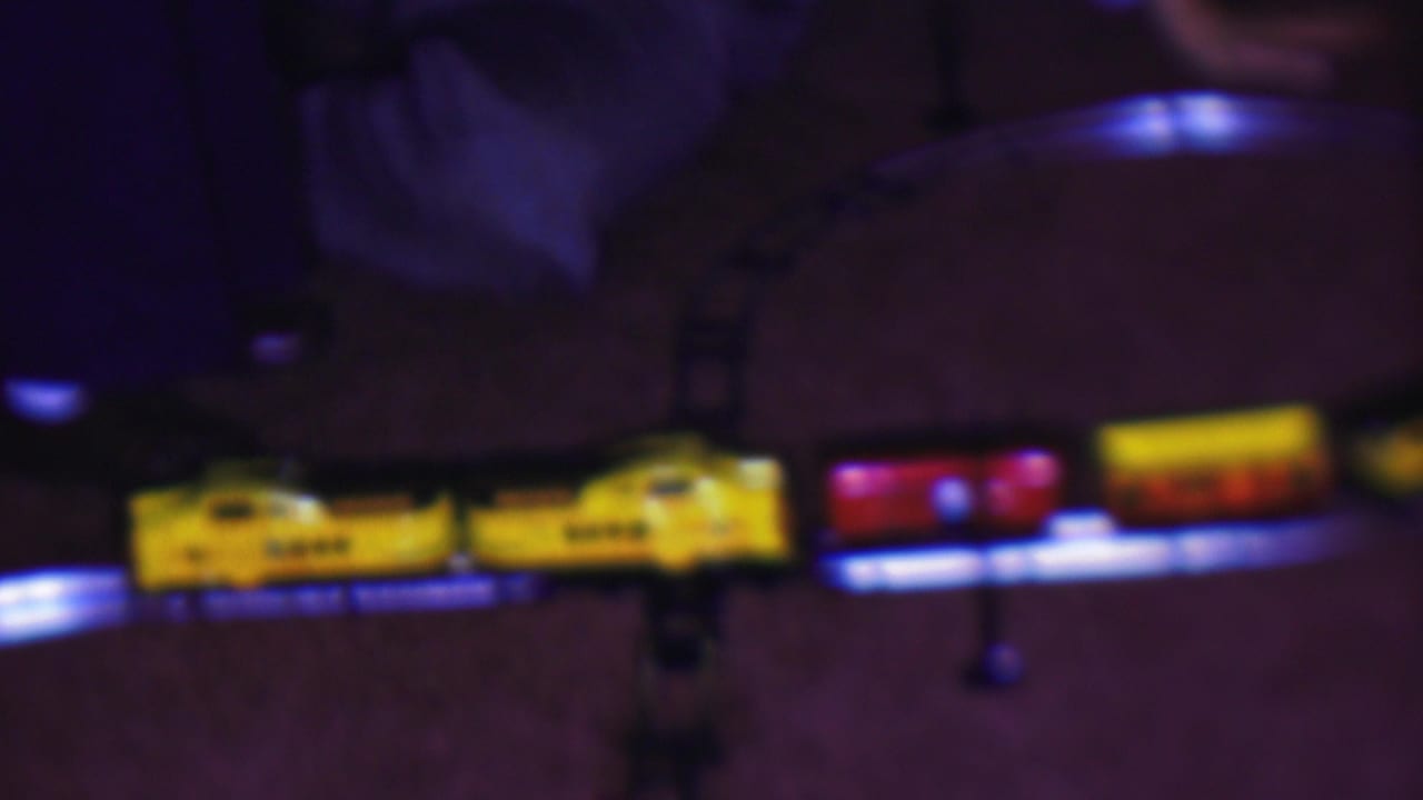 A yellow toy locomotive pulls red and yellow passenger cars along the curved track, captured in soft low-light 8mm texture inside a private interior.