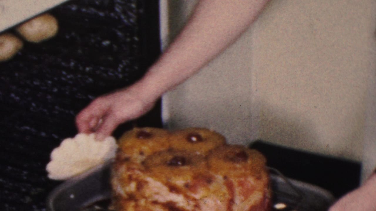 Hands guide a glazed ham in a roasting pan near the oven.