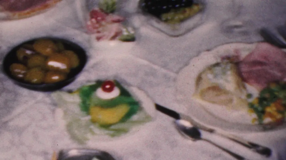 1953 Cleveland dining-table detail with a plate of ham or cold meat, a green dessert topped with a cherry, olives in a bowl, silverware, and a white tablecloth.