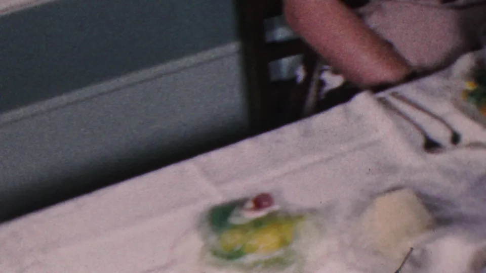 A formal dinner table in the Cleveland home-movie footage shows white linens, utensils, green gelatin desserts, and a partially visible diner seated at the edge of the frame.