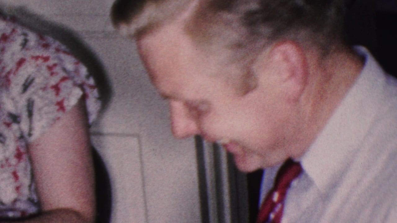 Man in striped shirt and red tie sits beside a woman in a floral dress at an indoor table.