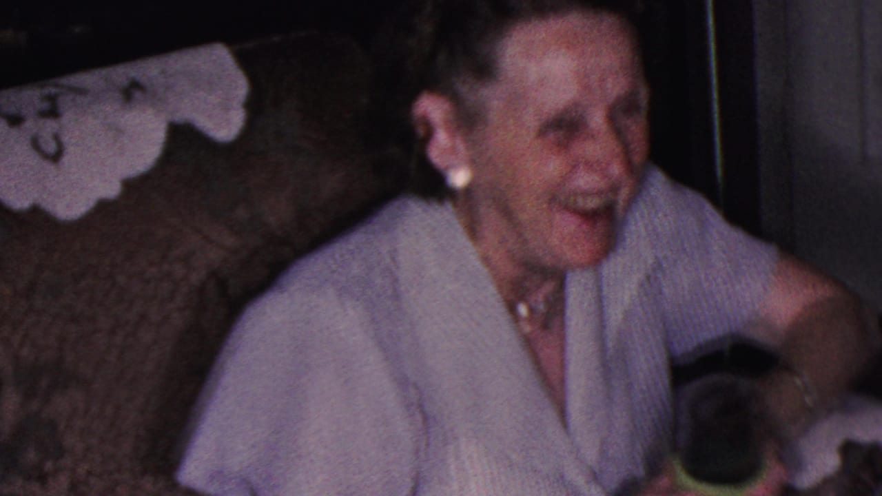 Older woman laughing on a couch while holding a green cup.