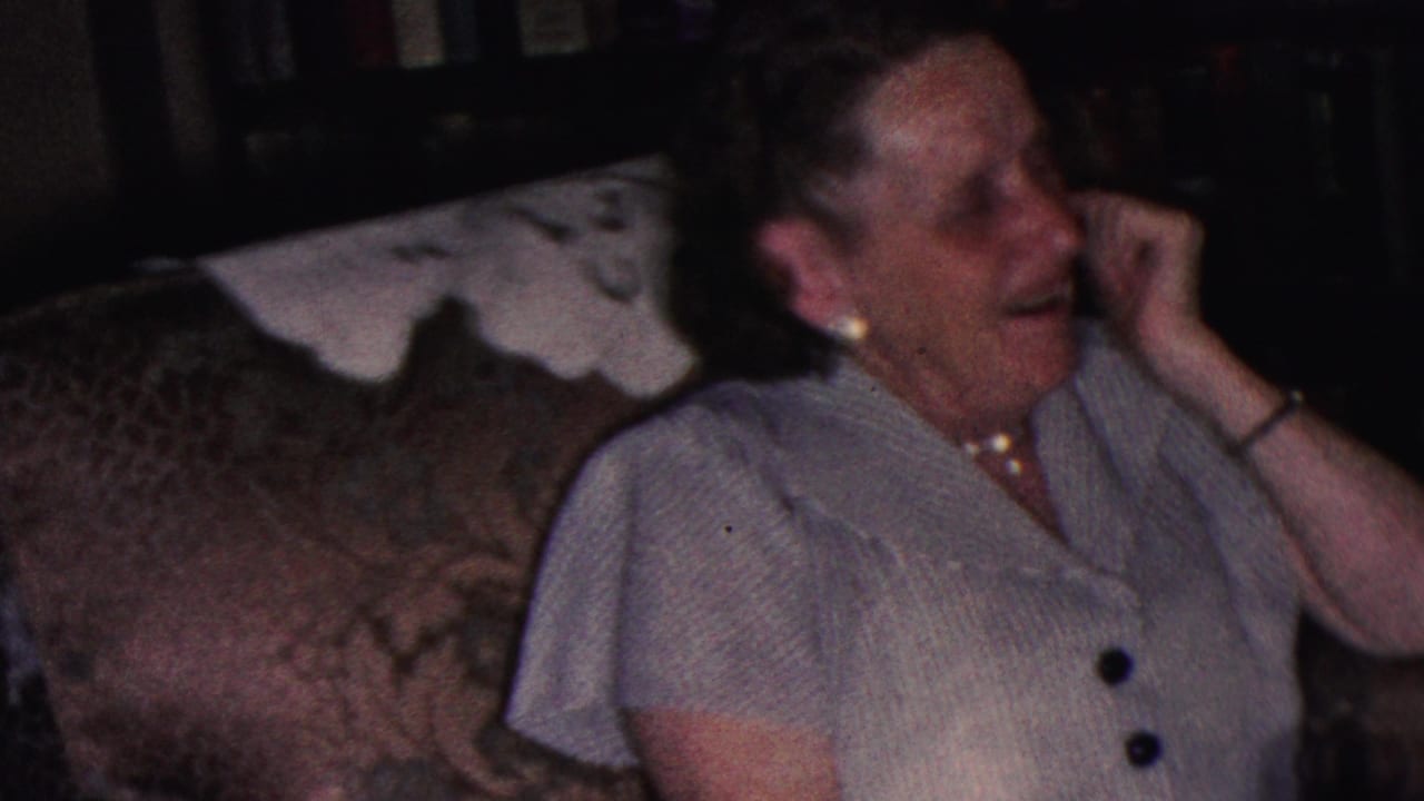 Woman on a couch turns to the side while laughing with her hand near her face.