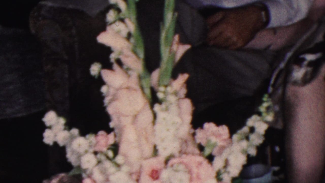Floral arrangement in the foreground with seated adults partly visible behind it.