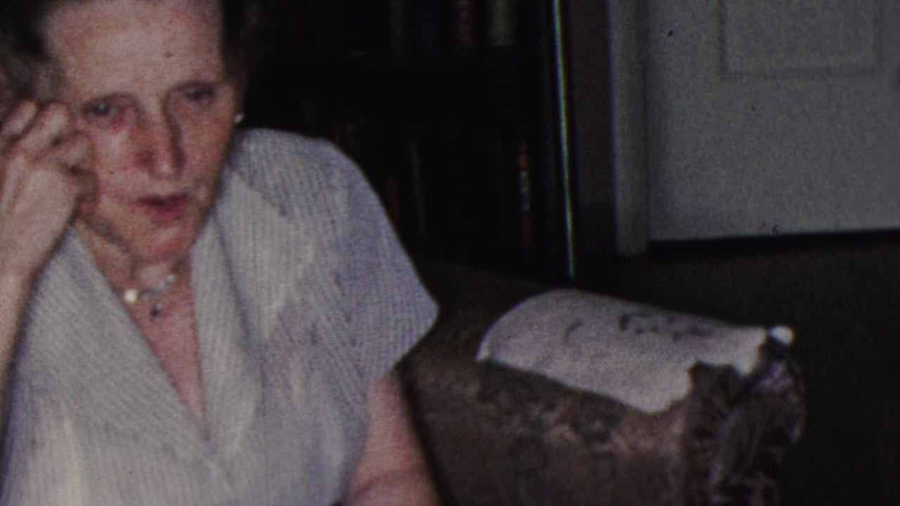 Elderly woman in a light striped blouse and pearl necklace seated in a dim private interior, identified by metadata as Cleveland, Ohio home-movie footage from 1953.