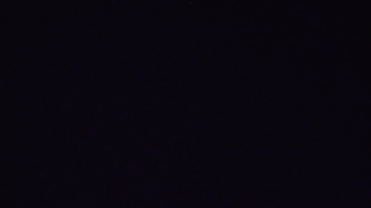 Very dark 8mm frame with only faint traces of the previous interior visible, likely near the end of the brief home-movie shot.