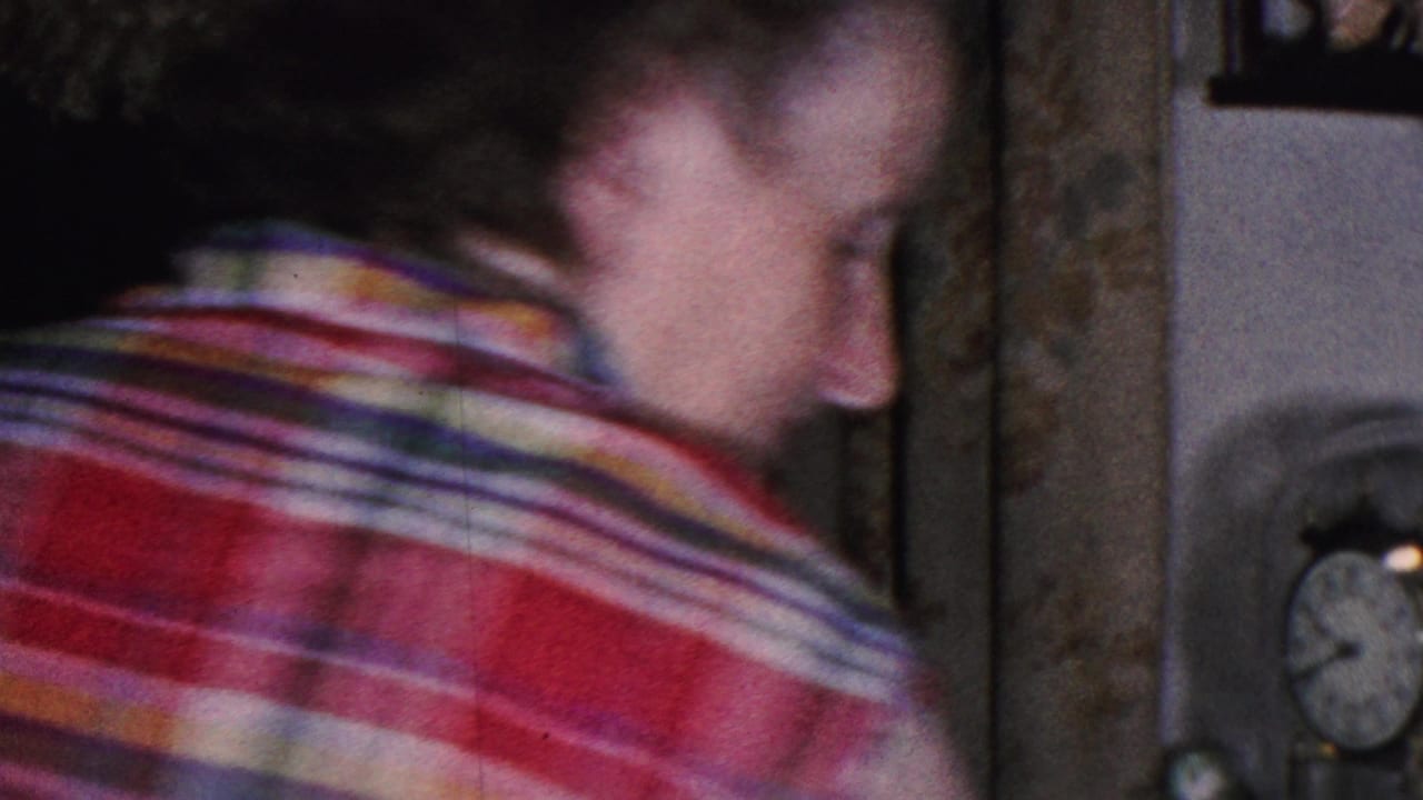 The woman is seen from the side and back in a dim Cleveland living room, with a mantel or shelf clock and framed wall decor visible nearby.
