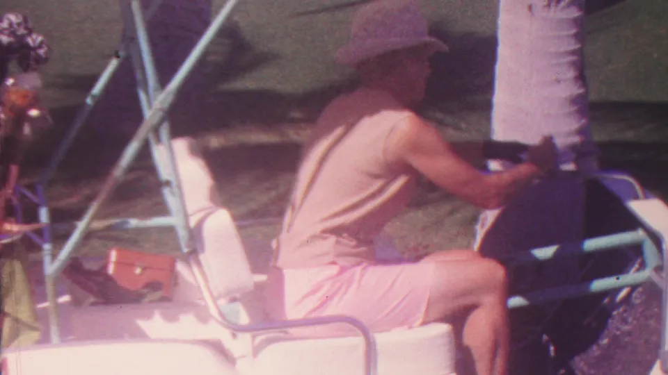 The 1962 Hawaii footage shows the man from the side, his hands near the steering wheel of a white golf cart as palm trunks and long shadows cross the course behind him.