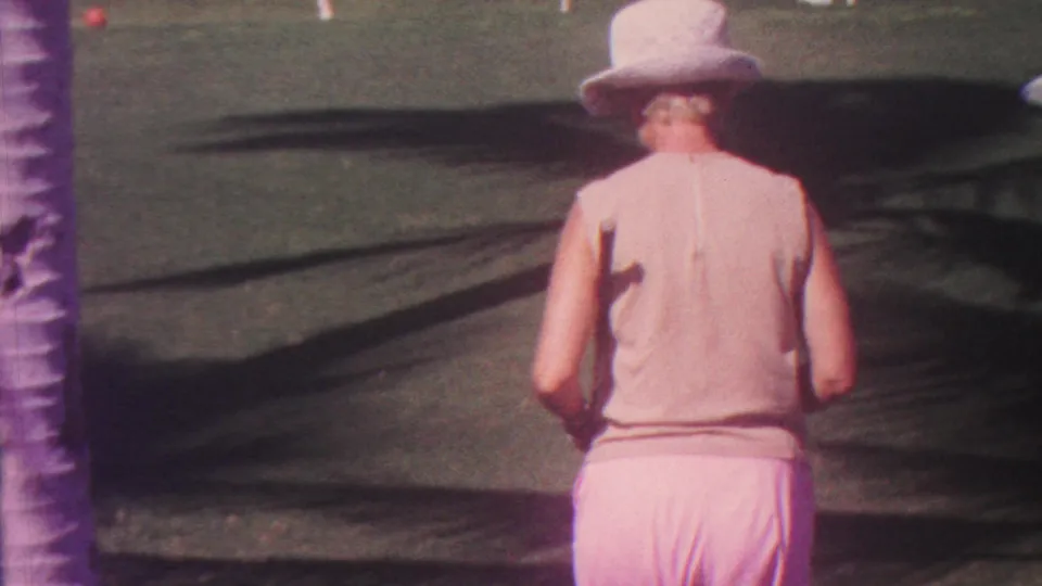The woman, filmed from behind in the 1962 Hawaii home movie, walks farther across the landscaped lawn while a small red croquet ball sits ahead near palm-shadowed grass.