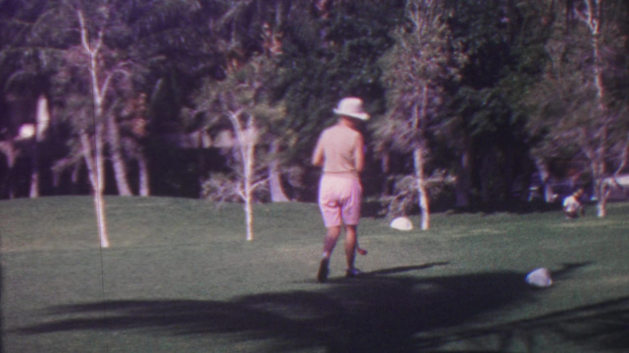 Golfer stands on a fairway near tee markers with trees behind.
