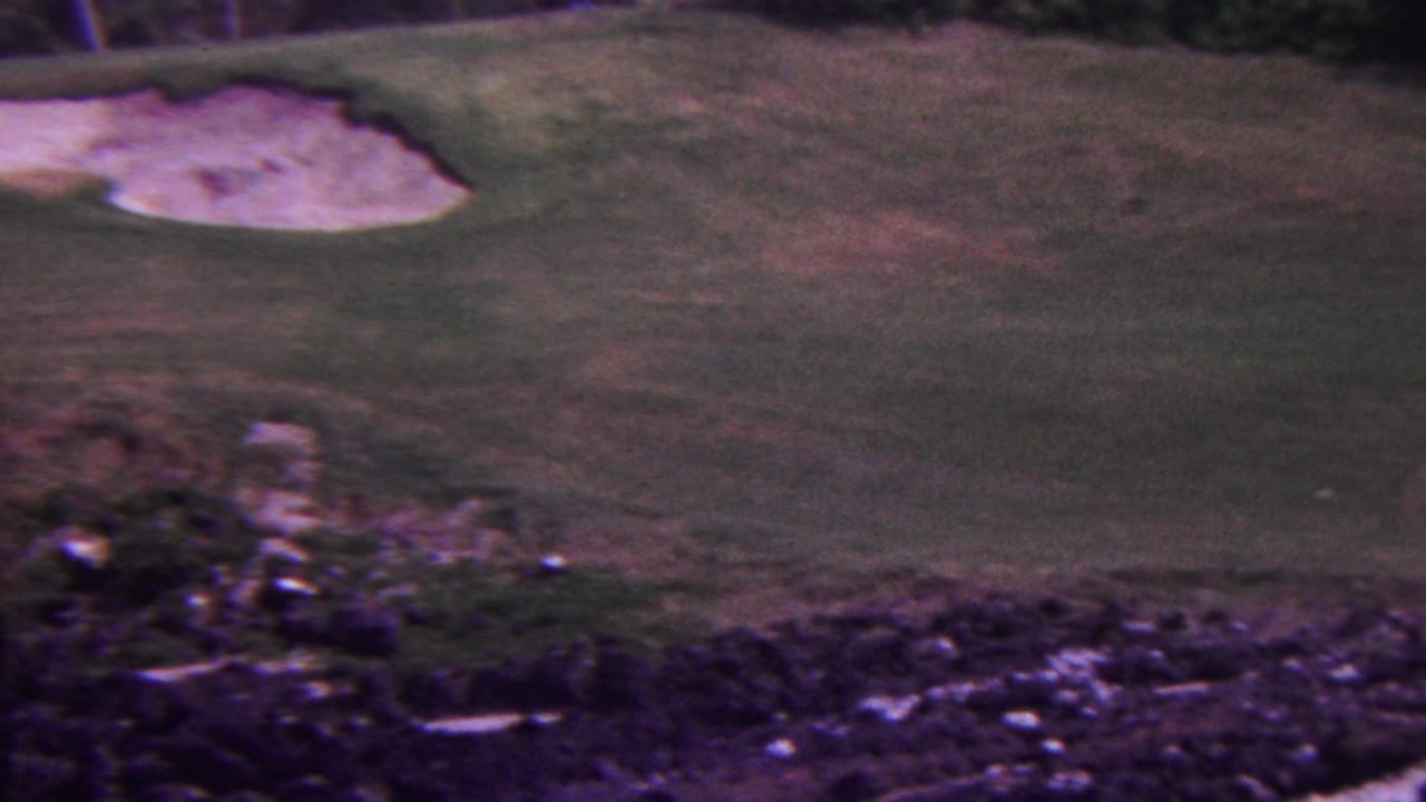1962 Hawaii 8mm frame showing a golf course fairway with pale sand bunkers, rocky terrain in the foreground, and dark vegetation along the upper edge.