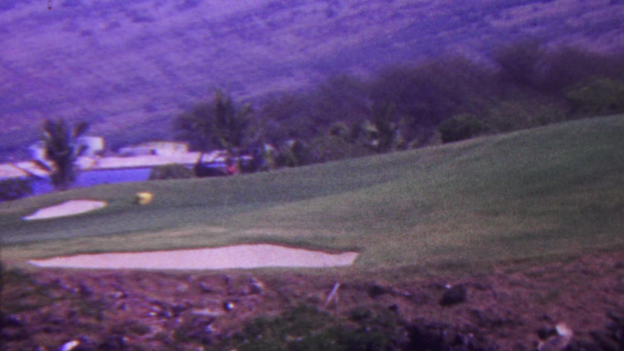 1962 Hawaii 8mm frame with a palm-lined golf course, blue water feature, white sand traps, and purple-tinged hills beyond the fairway.