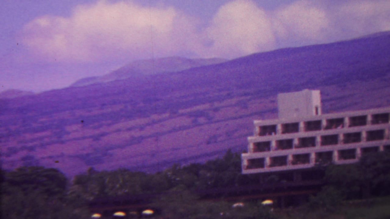 Modernist building at right with mountains, trees, and low clouds behind it.
