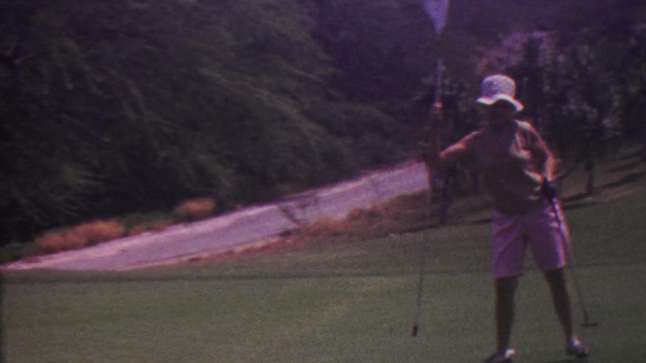 Woman golfer stands on the green with a club beside a flagstick and sloping path.