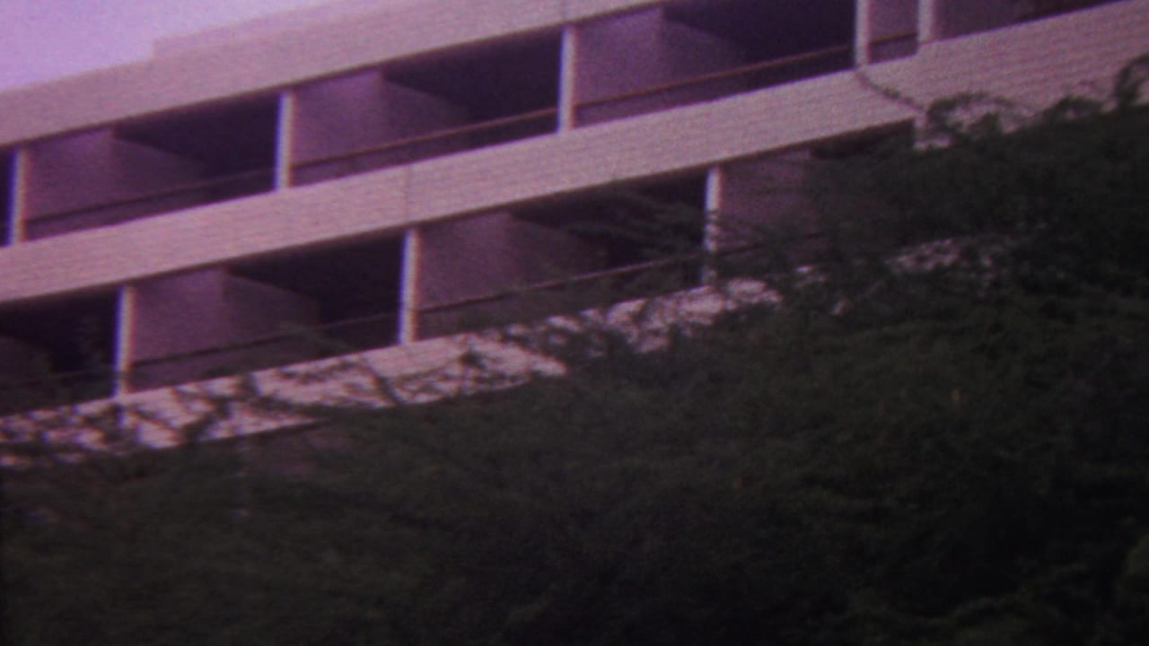 1962 Hawaii 8mm frame showing a white multi-story building with open balconies partly obscured by dense hillside vegetation.