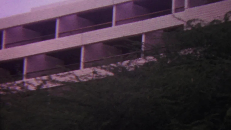 1962 Hawaii 8mm frame showing a white multi-story building with open balconies partly obscured by dense hillside vegetation.