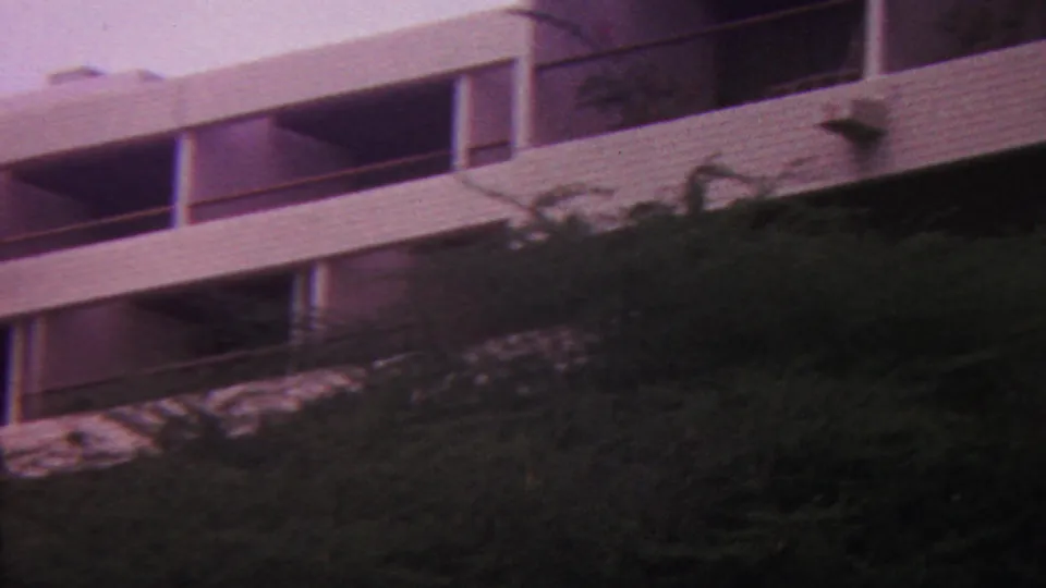 1962 Hawaii 8mm frame with a modernist white facade and repeating balcony openings seen above dark tropical greenery.