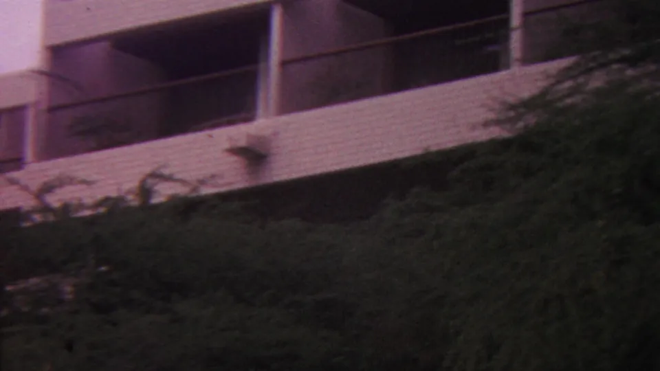1962 Hawaii 8mm frame showing a closer cropped view of balcony bays, railings, and white masonry partly blocked by hillside plants.