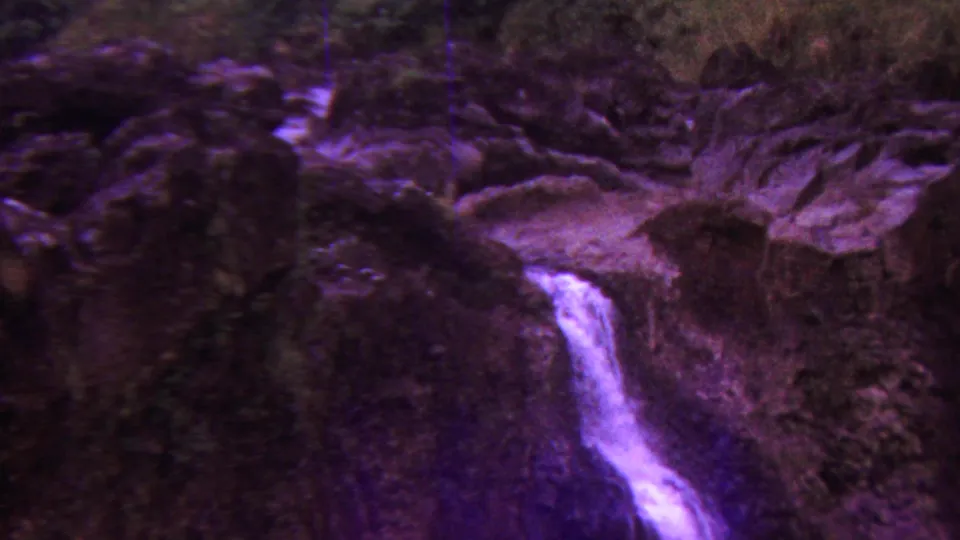 1962 Hawaii 8mm frame showing water cascading over dark volcanic-looking rocks, with visible film grain and purplish color shift.