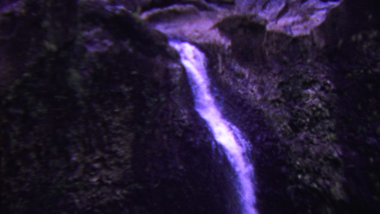 Waterfall stream cutting down a rocky cliff beside dark vegetation.