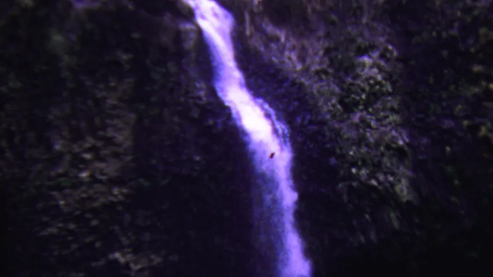 1962 Hawaii 8mm frame following the lower run of a narrow waterfall over dark mossy stone, with grain and color shift visible.