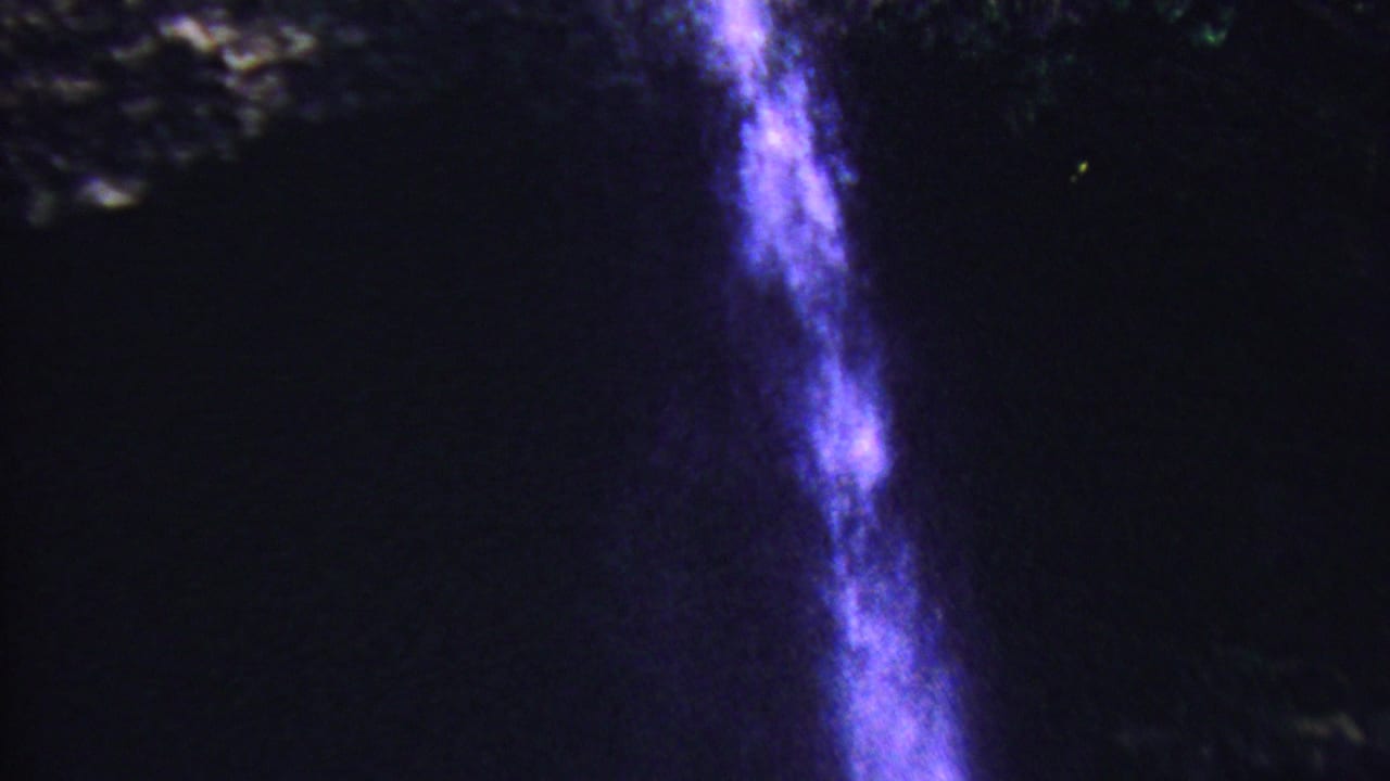 A bright vertical waterfall streak falls beside dark textured rock.
