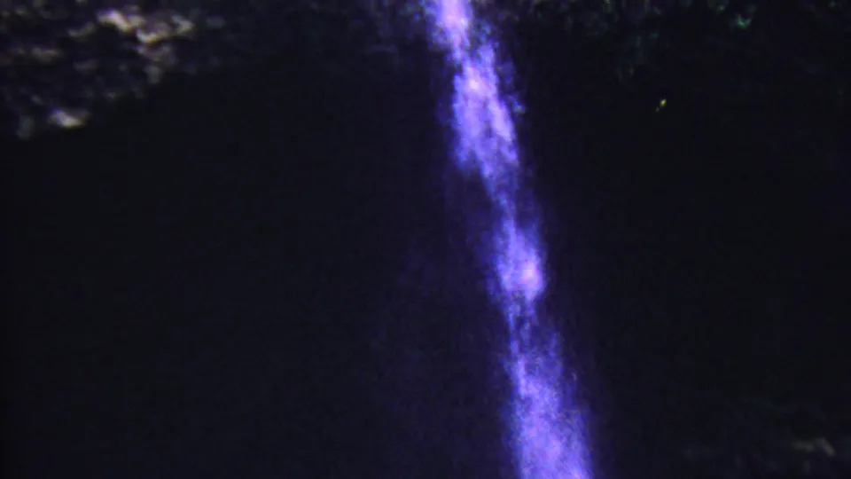 1962 Hawaii 8mm frame with a bright narrow waterfall streak running down beside shadowed cave-like rock and misty highlights.
