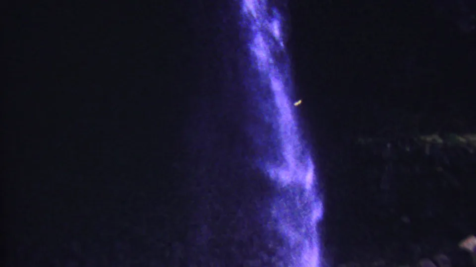 1962 Hawaii 8mm frame showing falling water entering a dark reflective pool beneath rough rock, with heavy shadow and purple color shift.