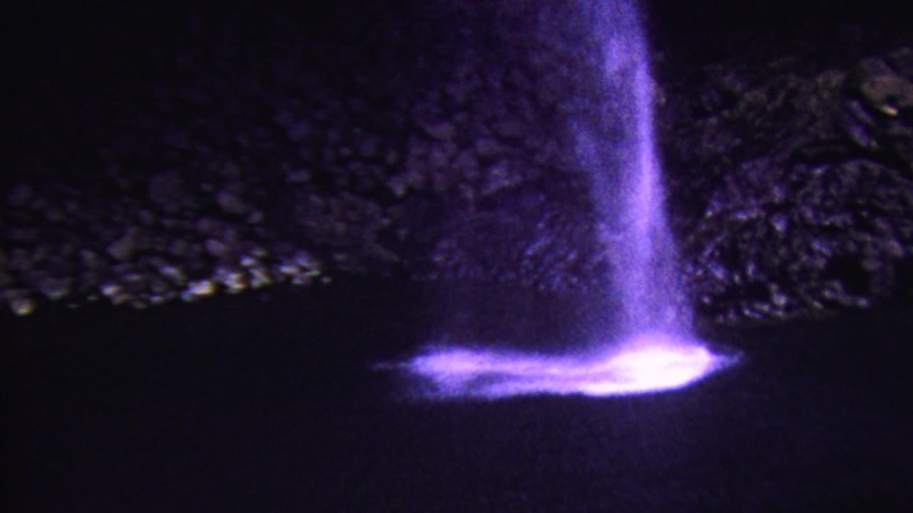 1962 Hawaii 8mm frame showing a violet-lit waterfall at night, with bright spray at the base and a dark rocky backdrop.