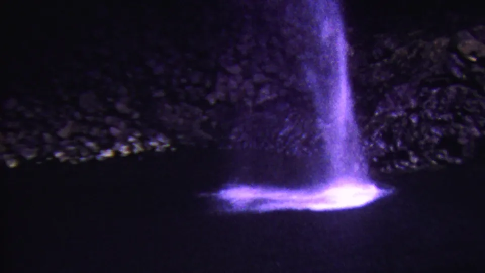 1962 Hawaii 8mm frame showing a violet-lit waterfall at night, with bright spray at the base and a dark rocky backdrop.