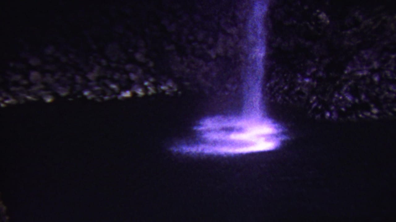 1962 Hawaii 8mm frame with a purple illuminated cascade falling beside dark rocks into a bright, shimmering base.