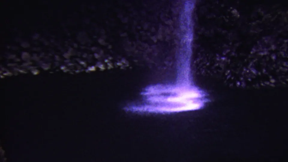 1962 Hawaii 8mm frame with a purple illuminated cascade falling beside dark rocks into a bright, shimmering base.